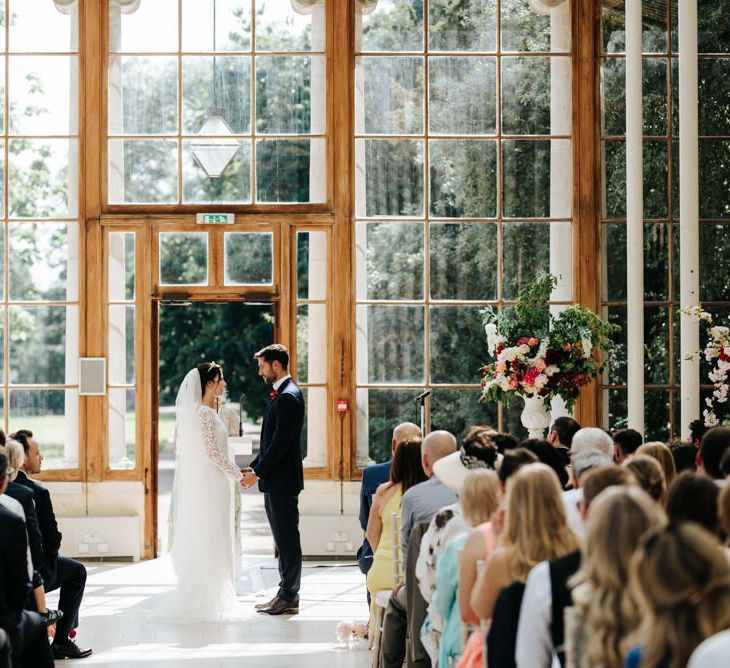 Bride and groom holding hands at the front of the aisle of Nash Conservatory at Kew Gardens