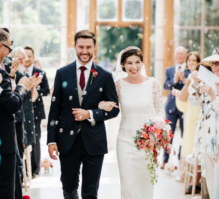 Bride and groom walk back down the aisle as a married couple while guests blow bubbles at them