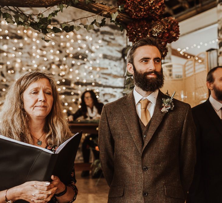 Groom in brown suit waits for bride at ceremony