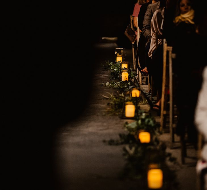 Candles and Foliage Lining Aisle | The Electrician’s Shop at Trinity Buoy Wharf | String Lights, Perspex Table Signs and Paper Cranes for Industrial Wedding | Frankee Victoria Photography