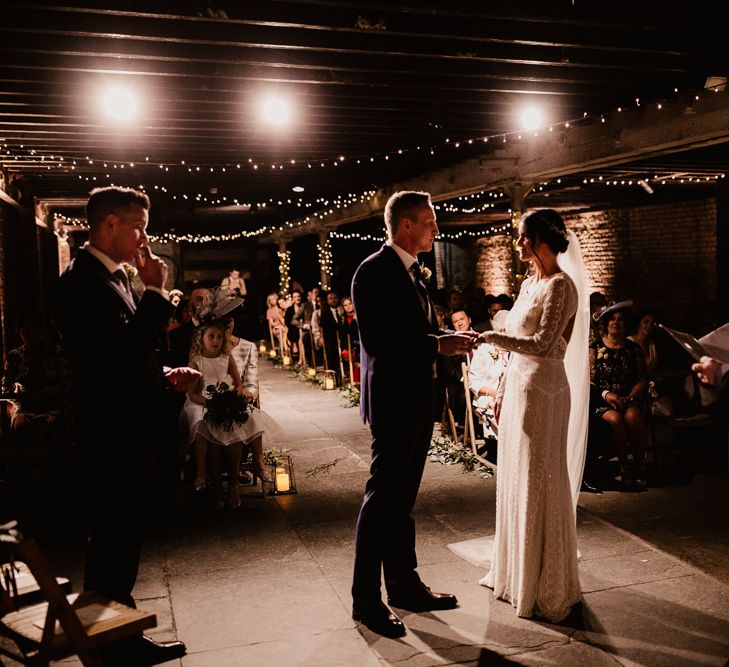 Bride in Lenora Dress by Wtoo Watters with Lace Sleeves and Keyhole Back | Prudence Halo Headpiece by Kelly Spence Wed | Floor Length Veil | Groom in Navy Suit with Grey Waistcoat from Jack Bunneys | Fairy Light Décor | Candle and Foliage Lined Aisle | Exposed Brick Industrial Venue | The Electrician’s Shop at Trinity Buoy Wharf | String Lights, Perspex Table Signs and Paper Cranes for Industrial Wedding | Frankee Victoria Photography