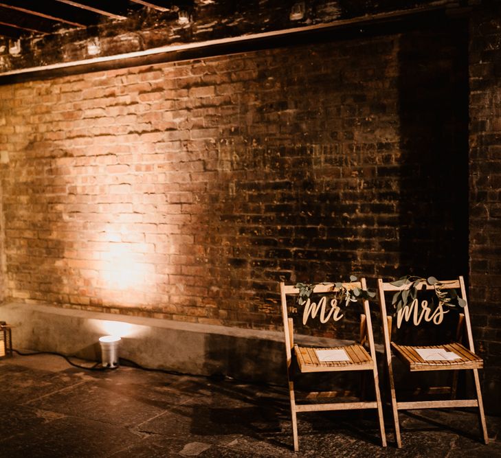 Wooden Chairs with Mr and Mrs Signs | Fairy Light Canopy | Exposed Brick Industrial Venue | The Electrician’s Shop at Trinity Buoy Wharf | String Lights, Perspex Table Signs and Paper Cranes for Industrial Wedding | Frankee Victoria Photography