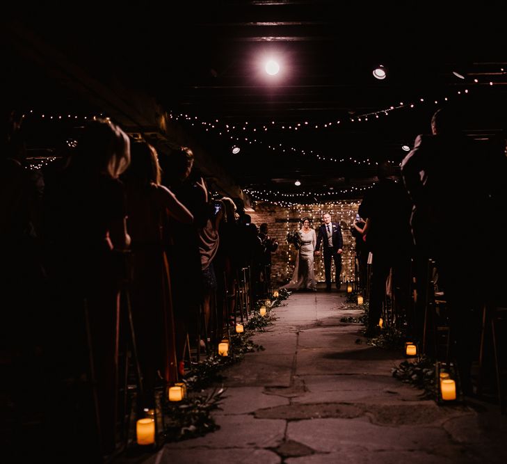 Bride in Lenora Dress by Wtoo Watters with Lace Sleeves and Keyhole Back | Prudence Halo Headpiece by Kelly Spence Wed | Floor Length Veil | Burgundy, Blush and White Flowers with Foliage and Ferns | Groom in Navy Suit with Grey Waistcoat from Jack Bunneys | Fairy Light Décor | Candle and Foliage Lined Aisle | Exposed Brick Industrial Venue | The Electrician’s Shop at Trinity Buoy Wharf | String Lights, Perspex Table Signs and Paper Cranes for Industrial Wedding | Frankee Victoria Photography