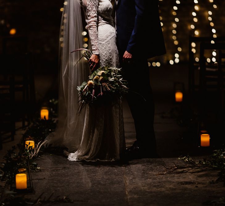 Bride in Lenora Dress by Wtoo Watters with Lace Sleeves and Keyhole Back | Floor Length Veil | Burgundy, Blush and White Flowers with Foliage and Ferns | Groom in Navy Suit with Grey Waistcoat from Jack Bunneys | Fairy Light Canopy | Candle and Foliage Lined Aisle | Exposed Brick Industrial Venue | The Electrician’s Shop at Trinity Buoy Wharf | String Lights, Perspex Table Signs and Paper Cranes for Industrial Wedding | Frankee Victoria Photography