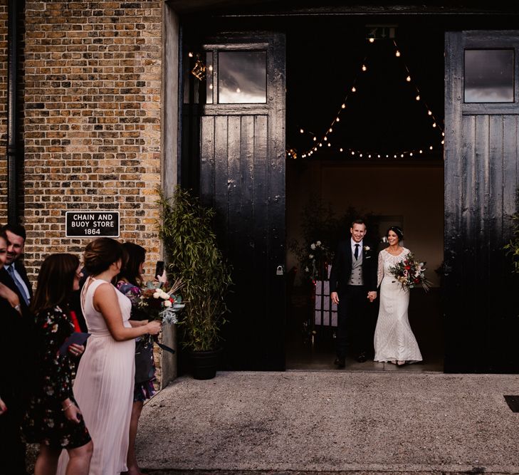 Bride in Lenora Dress by Wtoo Watters with Lace Sleeves and Keyhole Back | Prudence Halo Headpiece by Kelly Spence Wed | Floor Length Veil | Nude Valentino Rockstud Shoes | Burgundy, Blush and White Flowers with Foliage and Ferns | Groom in Navy Suit with Grey Waistcoat from Jack Bunneys | Trinity Buoy Wharf | String Lights, Perspex Table Signs and Paper Cranes for Industrial Wedding | Frankee Victoria Photography