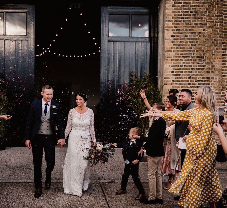 Bride in Lenora Dress by Wtoo Watters with Lace Sleeves and Keyhole Back | Prudence Halo Headpiece by Kelly Spence Wed | Floor Length Veil | Nude Valentino Rockstud Shoes | Burgundy, Blush and White Flowers with Foliage and Ferns | Groom in Navy Suit with Grey Waistcoat from Jack Bunneys | Trinity Buoy Wharf | String Lights, Perspex Table Signs and Paper Cranes for Industrial Wedding | Frankee Victoria Photography