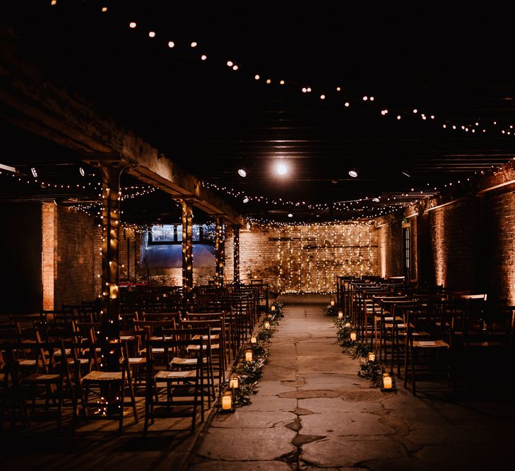 Fairy Light Canopy | Candle and Foliage Lined Aisle | Exposed Brick Industrial Venue | The Electrician’s Shop at Trinity Buoy Wharf | String Lights, Perspex Table Signs and Paper Cranes for Industrial Wedding | Frankee Victoria Photography