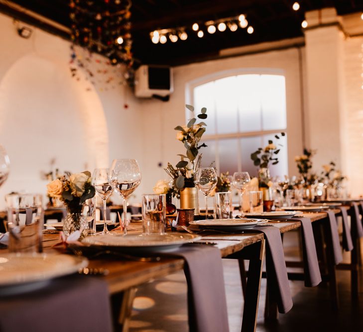 Wooden Trestle Tables | Grey Napkins | Festoon Lights | Hanging Paper Cranes | Flowers and Foliage in Gold Tin Cans | Paper Crane Place Settings | Trinity Buoy Wharf Wedding Venue | String Lights, Perspex Table Signs and Paper Cranes for Industrial Wedding | Frankee Victoria Photography