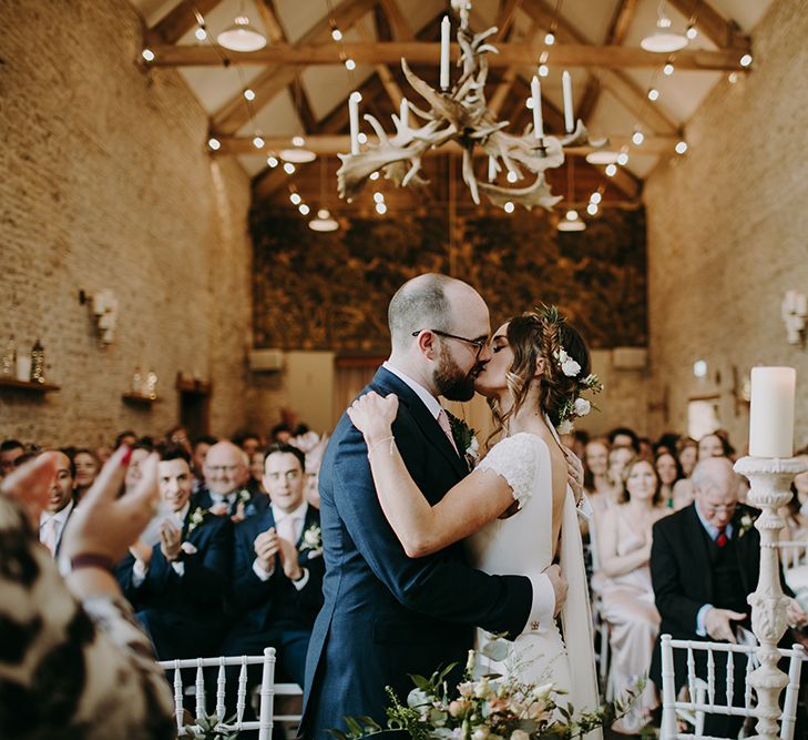 Bride in Pronovias Dralan Wedding Dress  and Groom in Navy Blue Moss Bros.  Suit Kissing During Wedding Ceremony