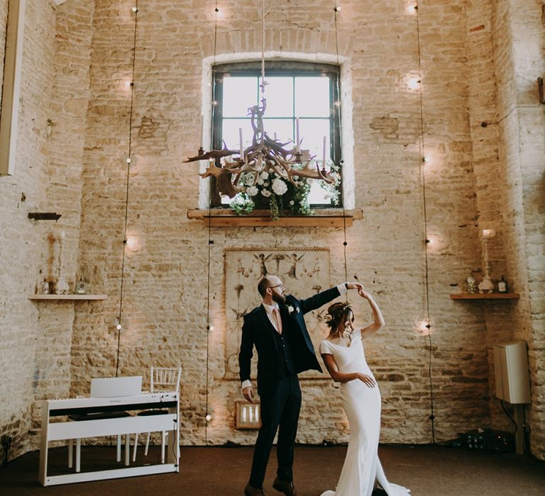 Groom in Navy Moss Bros. Suit Twirling His Bride in Pronovias Dralan Wedding Dress