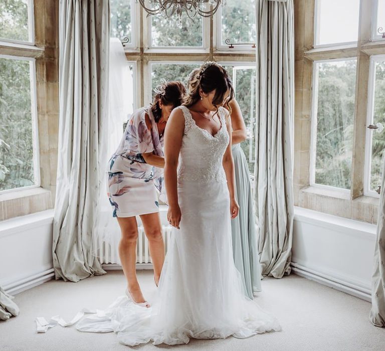 Bride getting into her laced dress with long train and soft curled hair styled with accessory