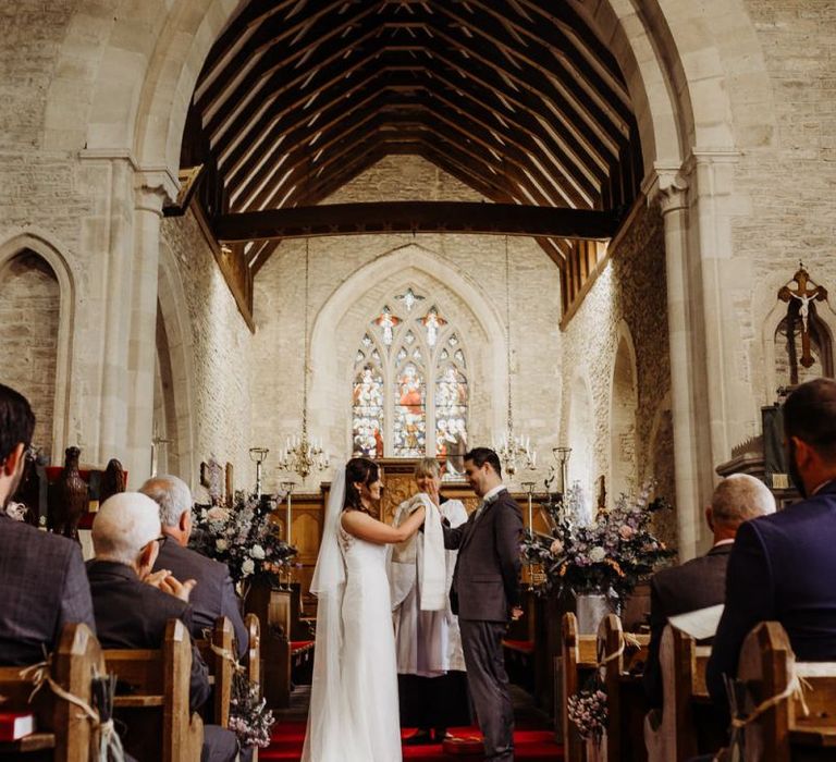 Bride and groom say their vows at church ceremony with laced bridal dress and long veil