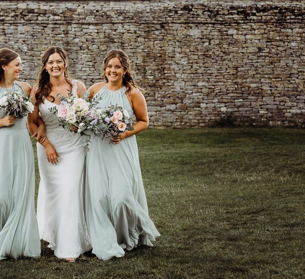 Bride wearing beautifully laced dress with her bridesmaids holding pastel floral bouquets