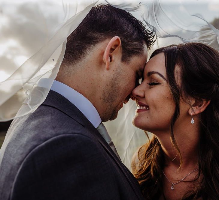 Bride and groom embrace featuring the brides beautiful veil and delicate earrings