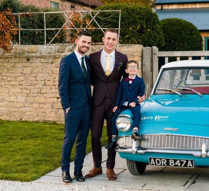 Grooms in Burgundy and Navy Remus Uomo Suits Standing Next to Ford Anglia Wedding Car