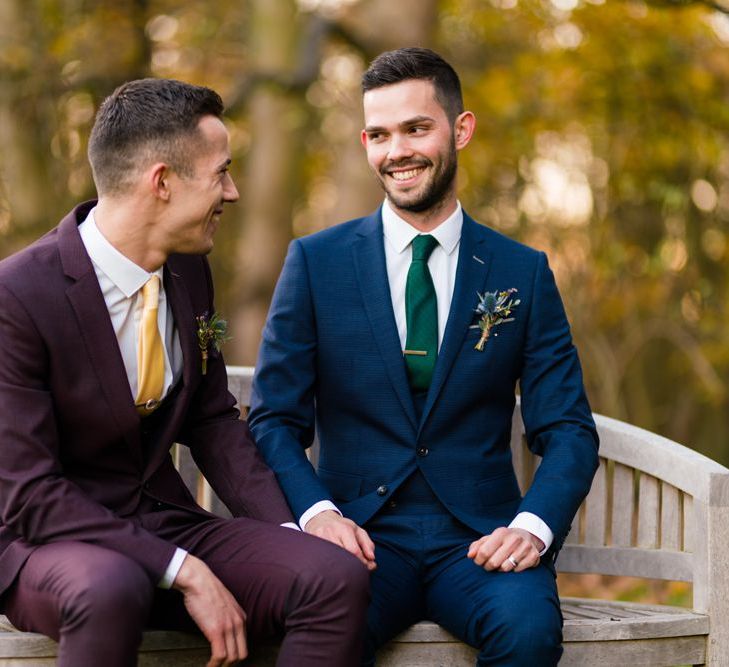 Two Grooms in Burgundy and Navy Remus Uomo Suits Sitting on a Bench