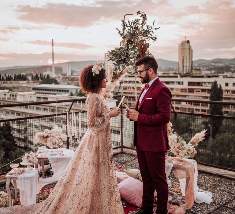 Bride and groom exchanging vows on a rooftop in sparkle wedding dress and burgundy suit