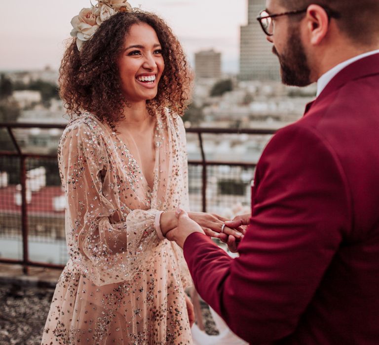 Bride in sparkle wedding dress smiling as her groom puts on her wedding ring