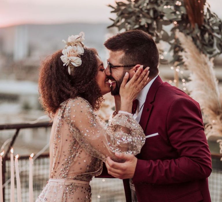 Bride in sparkle wedding dress kissing her groom in a red suit