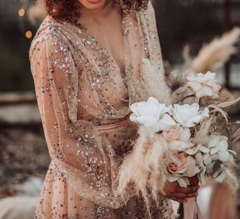 Boho bride in sparkle wedding dress with long sleeves and flowers in her curly hair