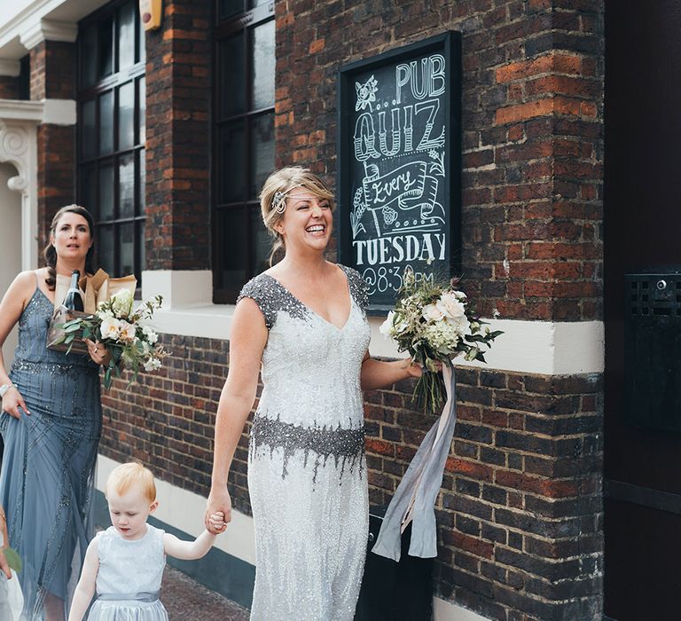 Bride in Embellished Shoulder Sequin Dress with Drop Waist by Eliza Jane Howell | 1920s Style Pearl Draping Headpiece | Bridal Bouquet with White Flowers, Foliage and Grey and Pink Trailing Ribbons | Strappy White Flat Sandals for Bride | Bridesmaid in Grey Strappy Dress with Sequins | Flower Girl in White Dress with Grey Sash | Metallic Confetti Cannons and Paper Lanterns with Bride in Beaded Shoulder Eliza Jane Howell Dress | Miss Gen Photography