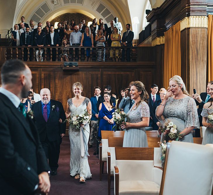 Bride in Embellished Shoulder Sequin Dress with Drop Waist by Eliza Jane Howell | 1920s Style Pearl Draping Headpiece | Bridal Bouquet with White Flowers, Foliage and Grey and Pink Trailing Ribbons | Strappy White Flat Sandals for Bride | Groom in Green and Blue Kilt | Bridesmaids in Mismatched Grey Dresses | Wedding Ceremony at Stoke Newington Town Hall | Metallic Confetti Cannons and Paper Lanterns with Bride in Beaded Shoulder Eliza Jane Howell Dress | Miss Gen Photography