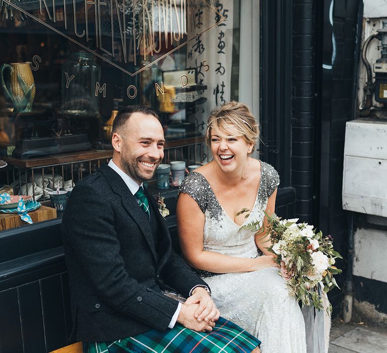 Bride in Embellished Shoulder Sequin Dress with Drop Waist by Eliza Jane Howell | 1920s Style Pearl Draping Headpiece | Bridal Bouquet with White Flowers, Foliage and Grey and Pink Trailing Ribbons | Strappy White Flat Sandals for Bride | Groom in Green and Blue Tartan Kilt | Metallic Confetti Cannons and Paper Lanterns with Bride in Beaded Shoulder Eliza Jane Howell Dress | Miss Gen Photography