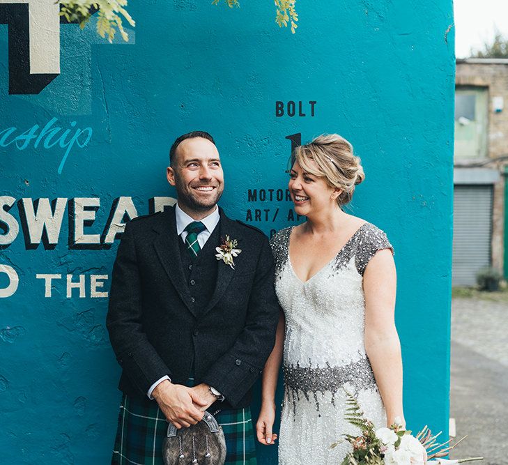 Bride in Embellished Shoulder Sequin Dress with Drop Waist by Eliza Jane Howell | 1920s Style Pearl Draping Headpiece | Bridal Bouquet with White Flowers, Foliage and Grey and Pink Trailing Ribbons | Groom in Green and Blue Tartan Kilt | Metallic Confetti Cannons and Paper Lanterns with Bride in Beaded Shoulder Eliza Jane Howell Dress | Miss Gen Photography