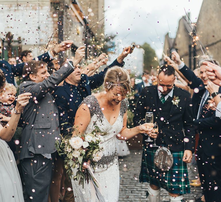 Confetti Cannon | Sparklers | Bride in Embellished Shoulder Sequin Dress with Drop Waist by Eliza Jane Howell | 1920s Style Pearl Draping Headpiece | Bridal Bouquet with White Flowers, Foliage and Grey and Pink Trailing Ribbons | Groom in Green and Blue Tartan Kilt | Clapton Country Club Wedding Reception | Metallic Confetti Cannons and Paper Lanterns with Bride in Beaded Shoulder Eliza Jane Howell Dress | Miss Gen Photography