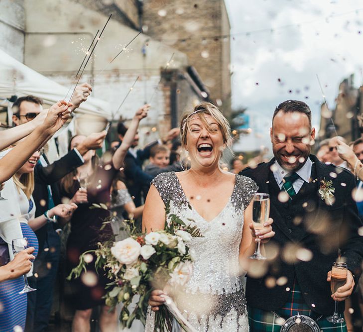 Confetti Cannon | Sparklers | Bride in Embellished Shoulder Sequin Dress with Drop Waist by Eliza Jane Howell | 1920s Style Pearl Draping Headpiece | Bridal Bouquet with White Flowers, Foliage and Grey and Pink Trailing Ribbons | Groom in Green and Blue Tartan Kilt | Clapton Country Club Wedding Reception | Metallic Confetti Cannons and Paper Lanterns with Bride in Beaded Shoulder Eliza Jane Howell Dress | Miss Gen Photography