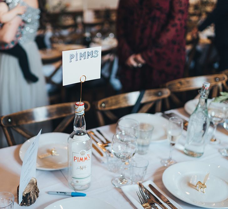 Banquet Tables | Wooden Chairs | Pimms Bottle Table Sign | Log Slice Displaying Wedding Breakfast Menu | Gold Giraffe Place Settings | Wedding Reception at Clapton Country Club | Metallic Confetti Cannons and Paper Lanterns with Bride in Beaded Shoulder Eliza Jane Howell Dress | Miss Gen Photography