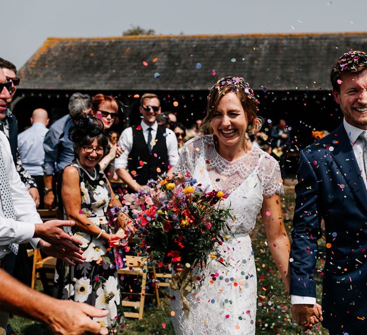 Colourful Confetti Moment with Bride in Lace Made with Love Wedding Dress and Groom in Navy Suit