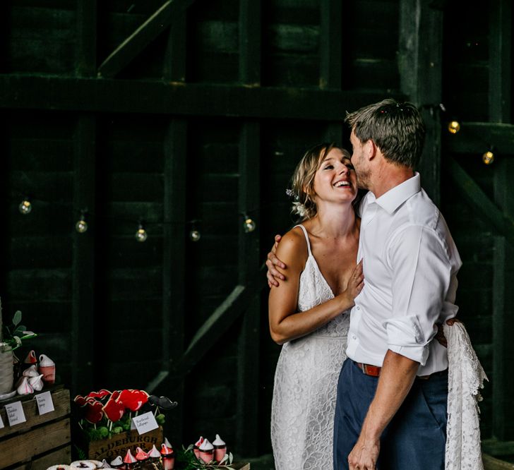 Bride and Groom Embracing Next to Their Dessert Table