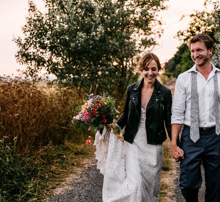 Bride in Made with Love Lace Wedding Dress and Groom in Godfather Tailoring Hand in Hand During Sunset