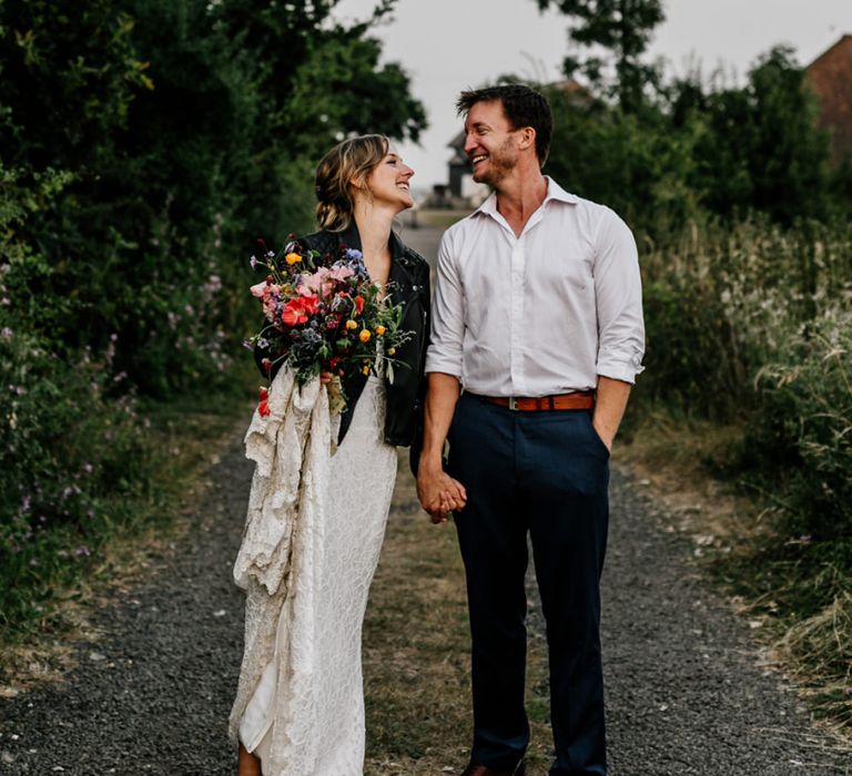 Bride in Made with Love Lace Wedding Dress and Leather Jacket and Groom in Godfather Tailoring Walking Hand in Hand