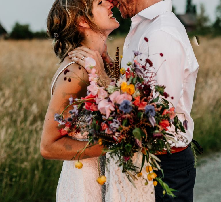 Bride in Made with Love Lace Wedding Dress holding a Colourful Bouquet and Groom in Godfather Tailoring