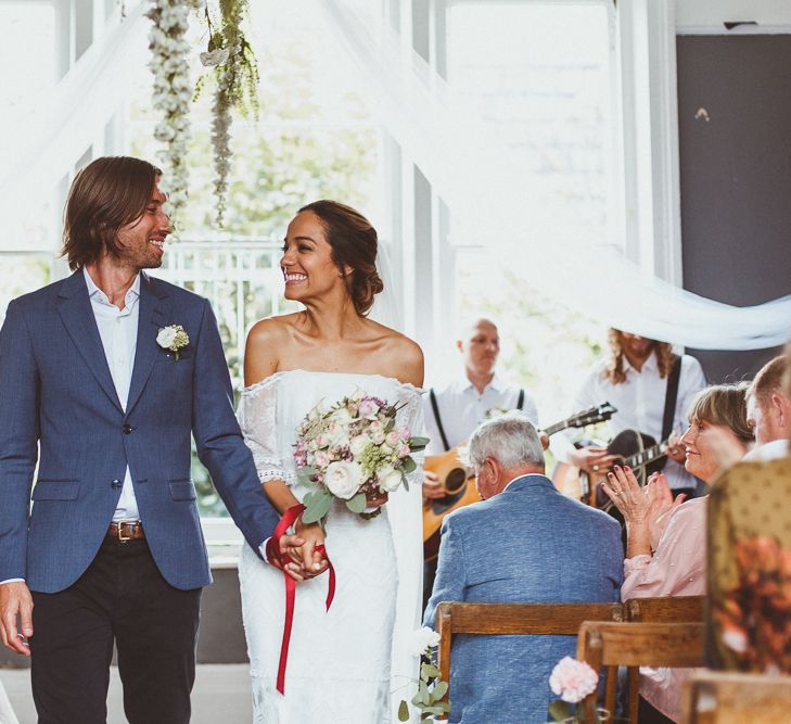 Happy Bride and Groom Just Married with Bride in 'Emanuela' Grace Loves Lace Wedding Dress and Groom in Black Trousers, White Shirt and Blue Blazer