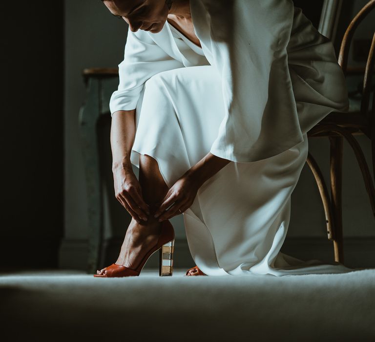 Bride wearing statement red heels tucked under elegant dress at winter wedding