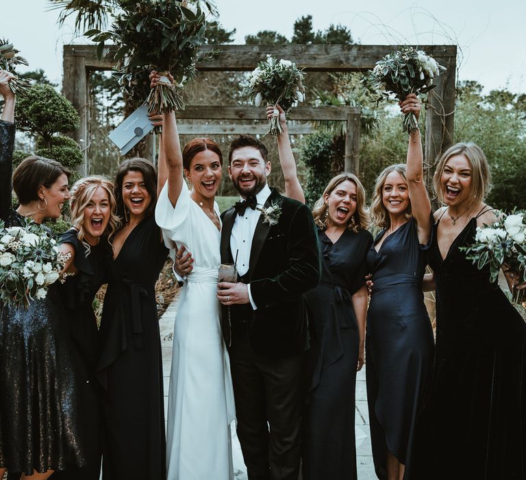 Bride and groom with  her bridesmaids wearing black dresses and white floral bouquets