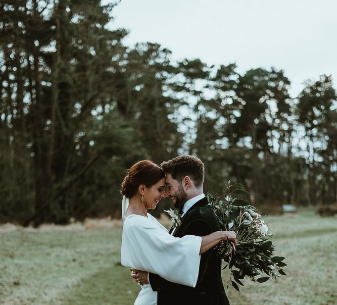 Bride and groom embrace at winter wedding wearing custom made three piece velour suit