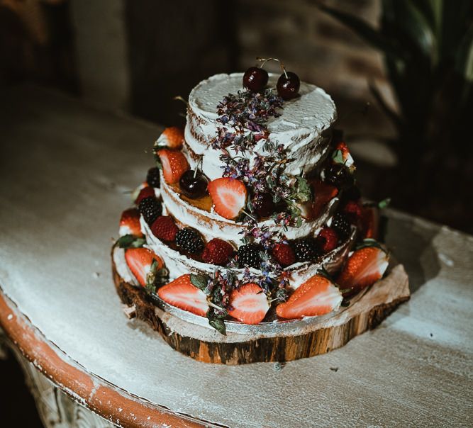 Semi-naked rustic wedding cake with fresh berries served on a tree stump