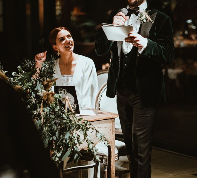 Bride and groom enjoy the speeches at winter reception with foliage styling  and winter decor