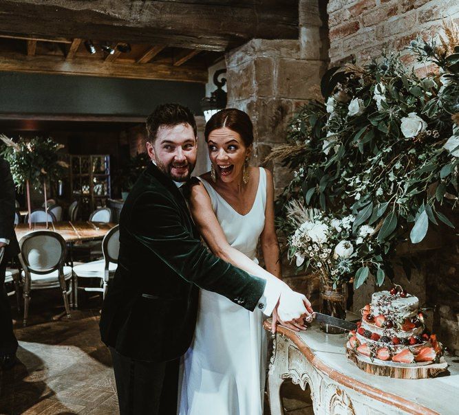 The couple cut the semi-naked cake with rustic styling and fresh berries