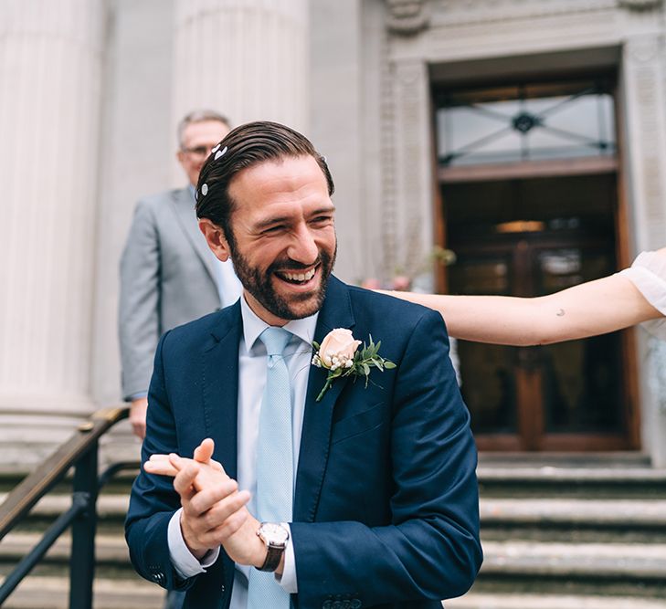 Groom in navy suit and blue tie covered in confetti