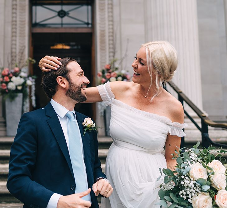 Bride in maternity wedding dress picking confetti from her grooms hair