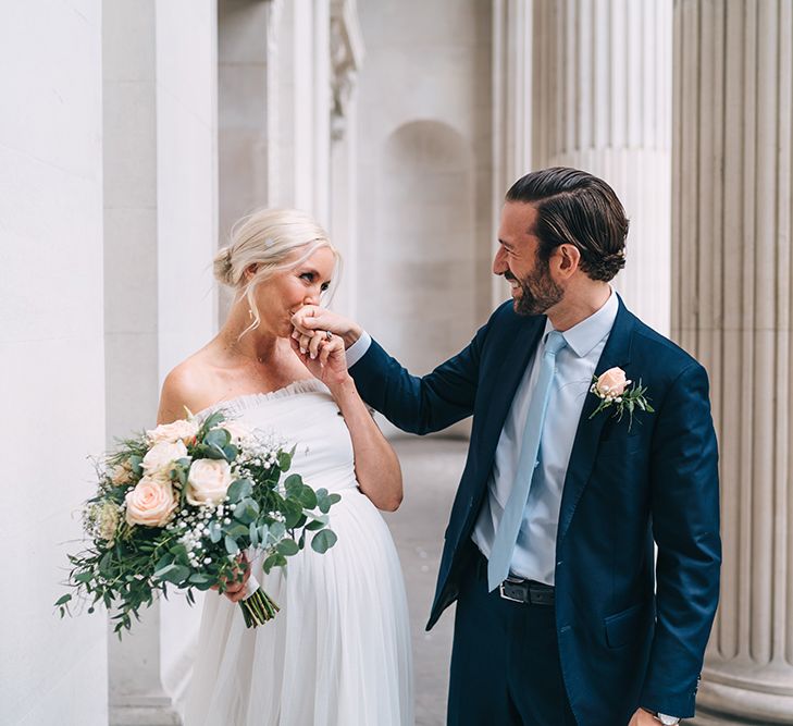 Pregnant bride in maternity wedding dress kissing her grooms hand