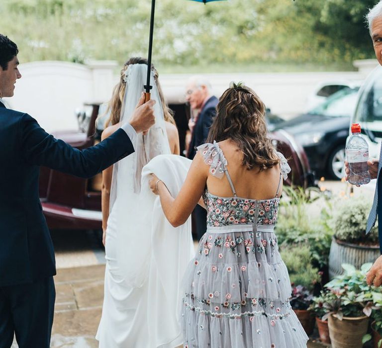 Bridesmaid in Needle and Thread Dress Holding The Brides Train as She Gets into the Wedding Car