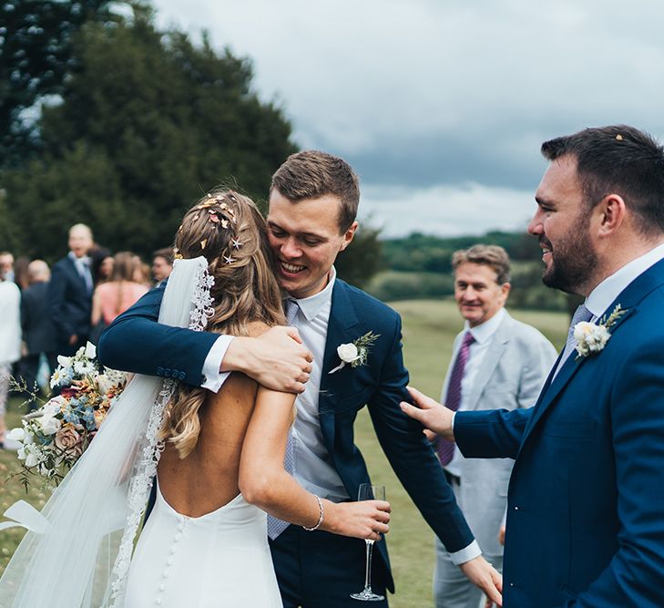 Wedding Guest Hugging The Bride in a Backless Made With Love Wedding Dress and Lace Edge Veil