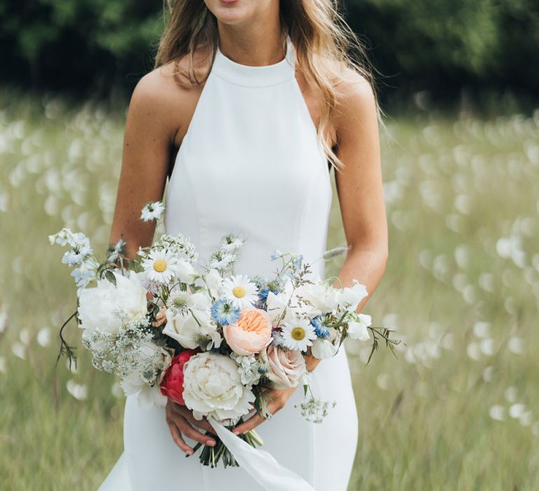 Bride in Halterneck Made With Love Wedding Dress Holding a White Peony and Pastel Flower Bouquet in a Field