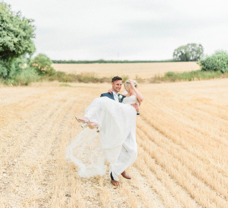 Groom in Moss Bros. Navy Suit Picking Up his Bride in a Lace Wedding Dress and Cathedral Veil